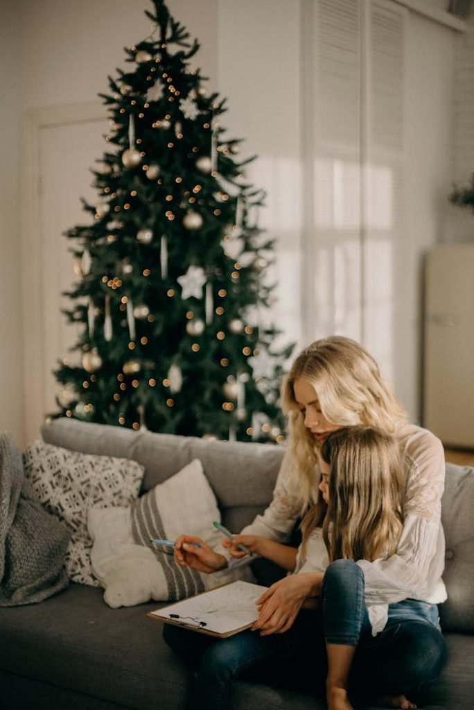A mother and daughter enjoy a cozy moment by the Christmas tree indoors.